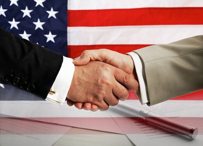 two people shaking hands in front of an American flag